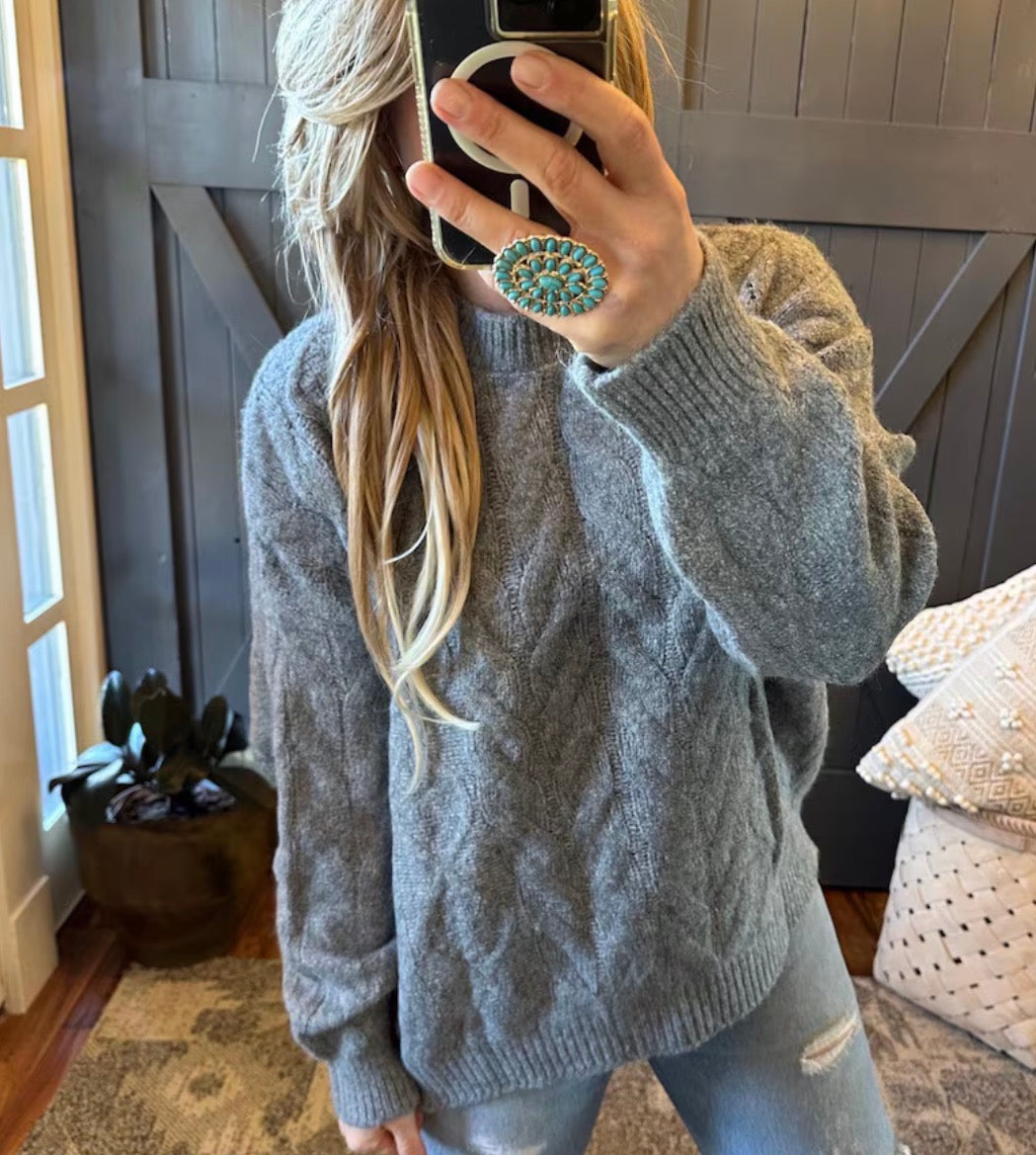 Person wearing a gray cable knit sweater taking a mirror selfie.