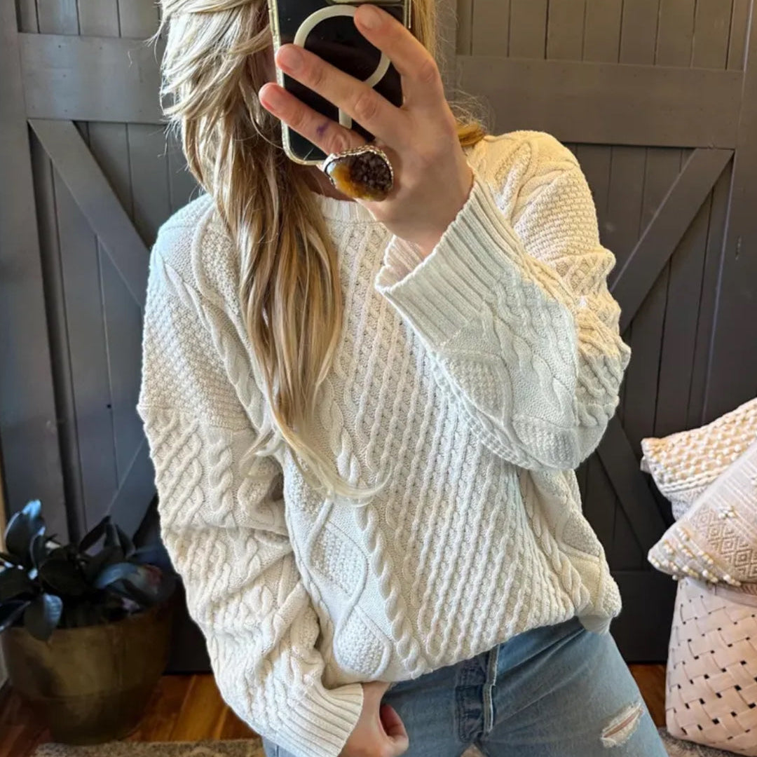 Person wearing a white cable knit sweater taking a mirror selfie.