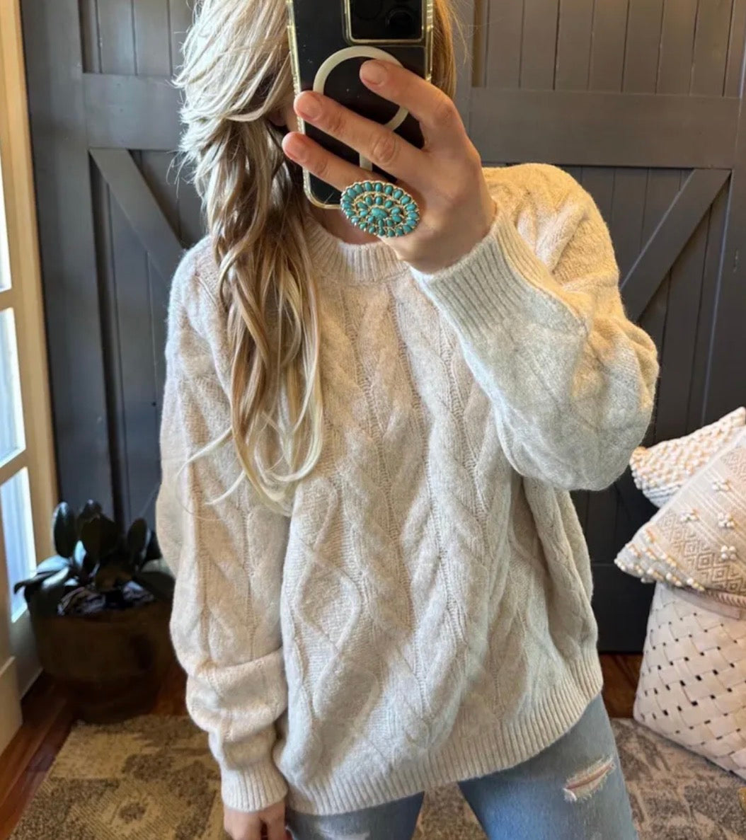 Person wearing a white cable knit sweater taking a mirror selfie.