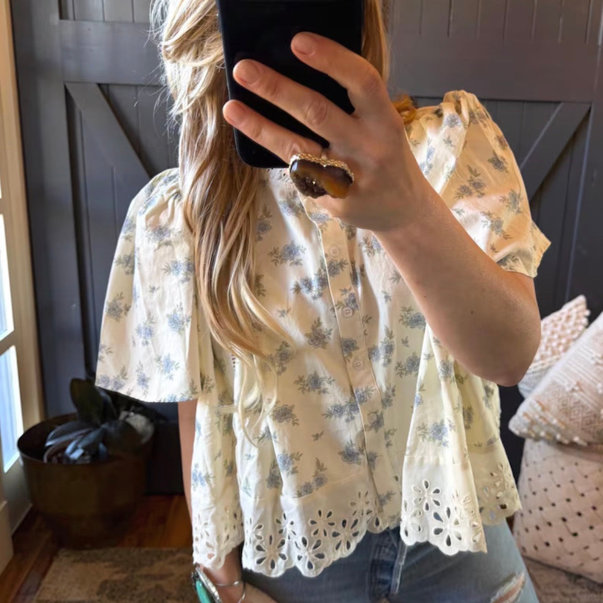 Person wearing a floral blouse taking a mirror selfie.