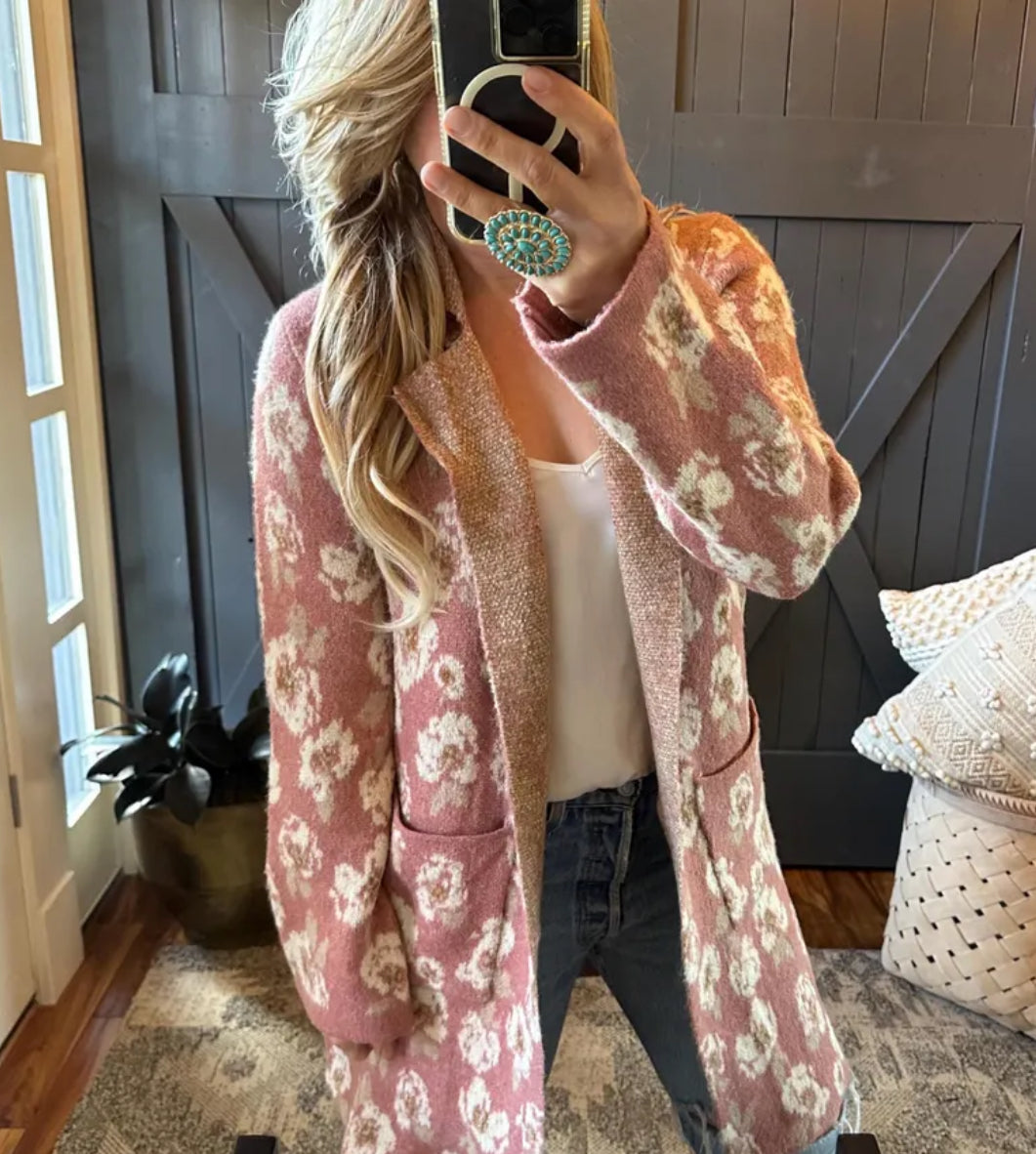 Person wearing a pink floral cardigan in a room with wooden walls and a rug.