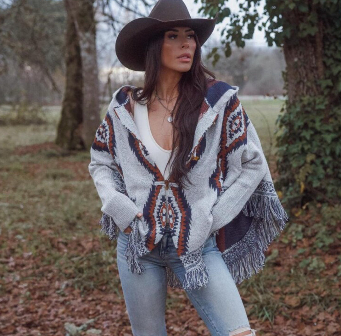 Woman wearing a patterned cardigan and cowboy hat in a forest setting