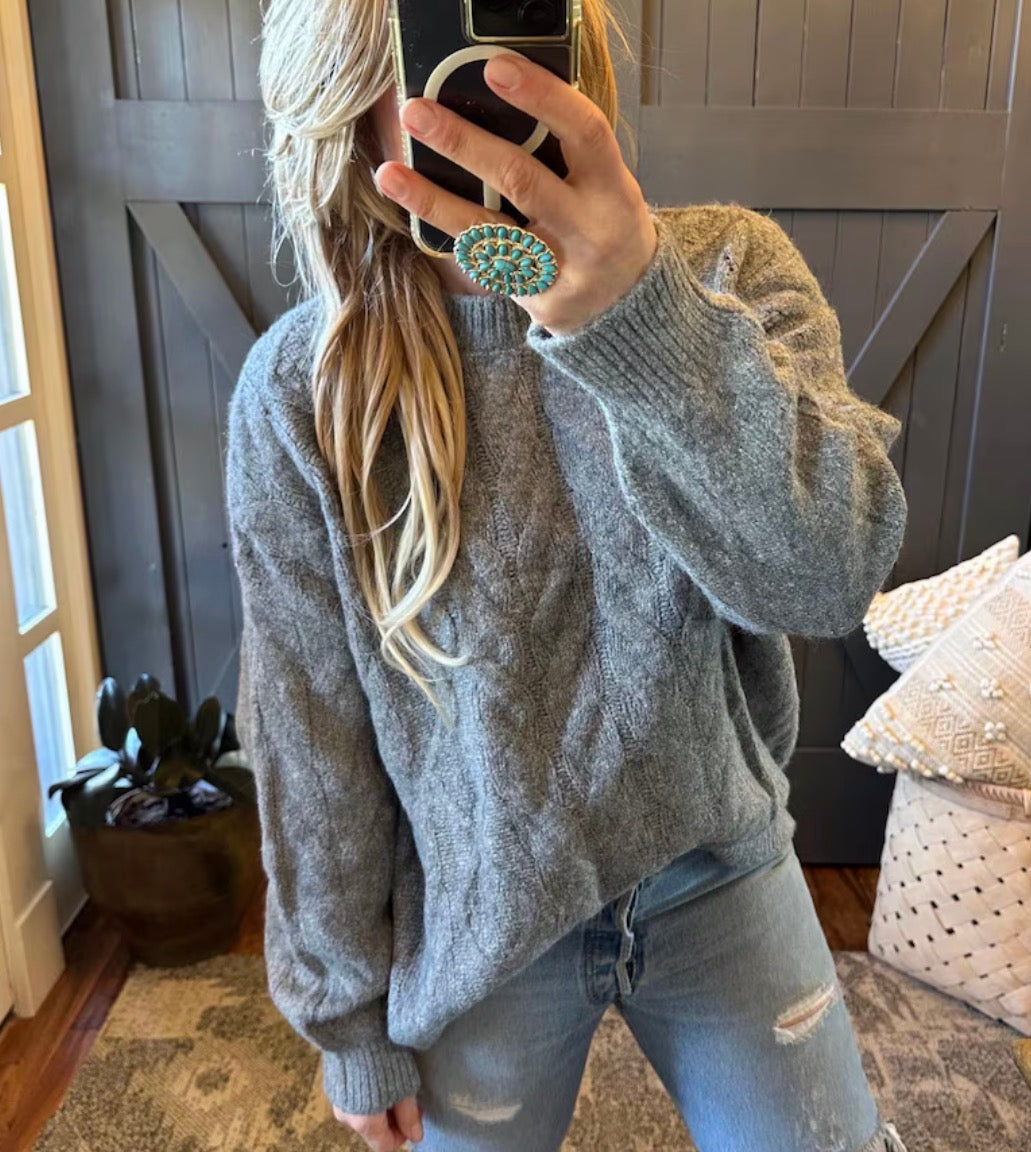 Person wearing a gray sweater and light blue jeans taking a mirror selfie.