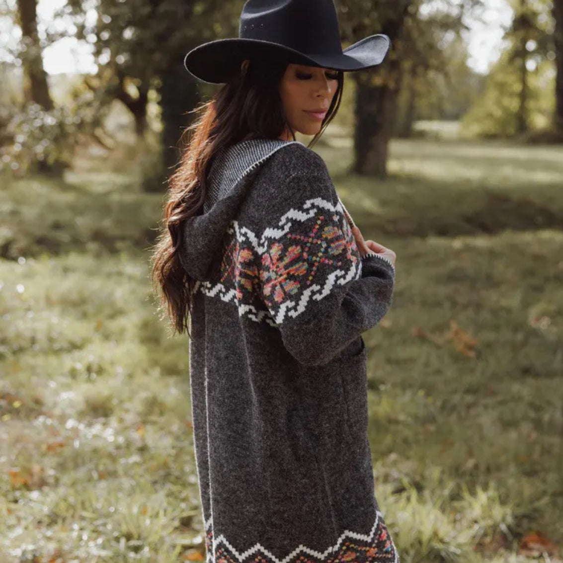 Woman wearing a patterned cardigan and black hat in a forest setting