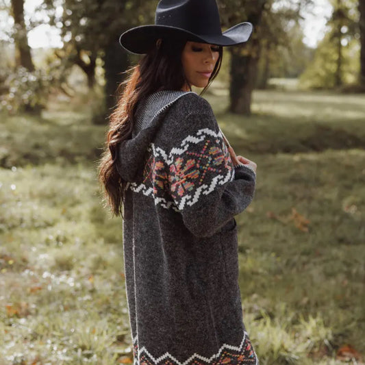 Woman wearing a patterned cardigan and black hat in a forest setting