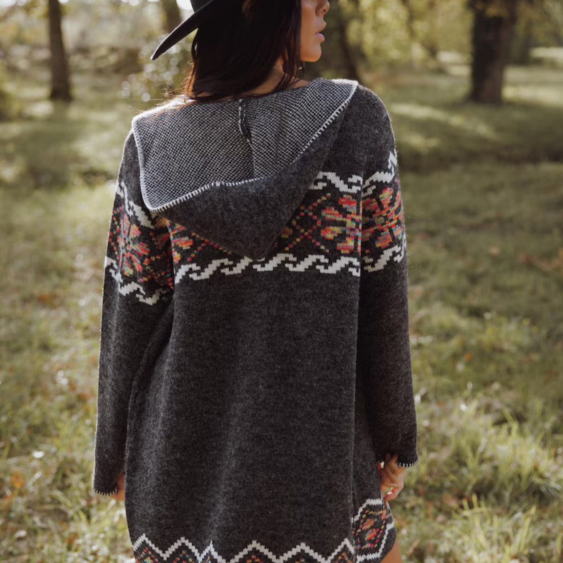 Person wearing a dark gray hooded sweater with colorful patterns in an outdoor setting
