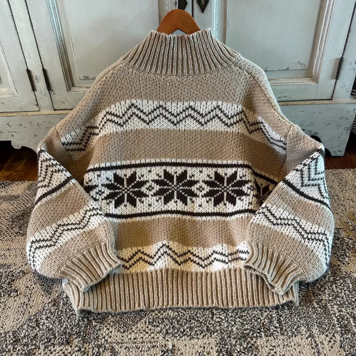 Beige sweater with pattern on a wooden hanger against a rustic background