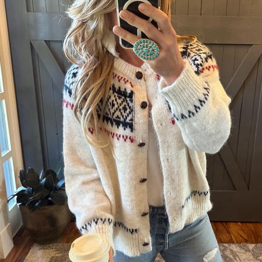 Person wearing a patterned cardigan taking a mirror selfie indoors.