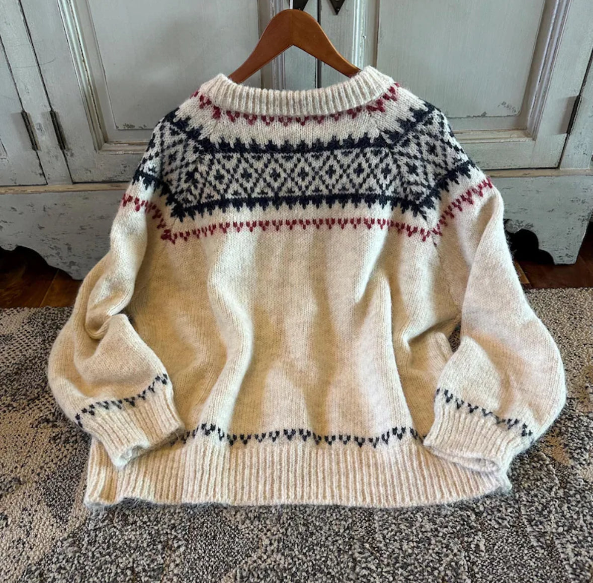 Beige sweater with patterned neckline on a wooden hanger against a white wall.