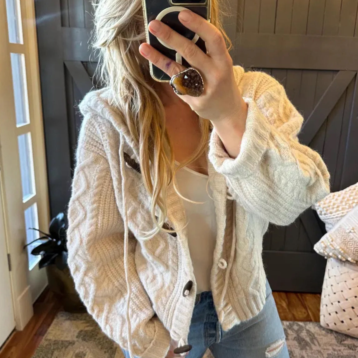 Person wearing a beige knitted cardigan taking a mirror selfie.