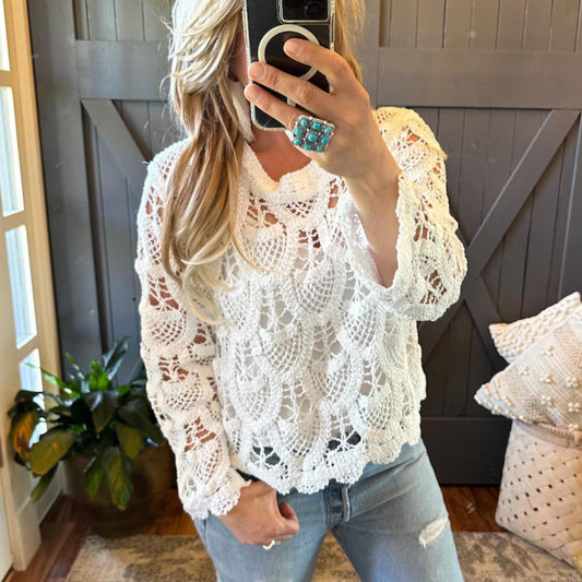 Person wearing a white lace top and jeans in a room with a plant and pillow.