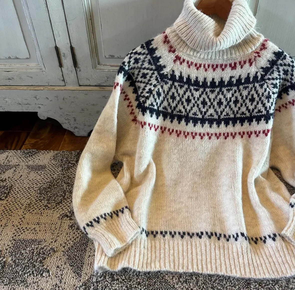 Cream-colored sweater with black and red pattern on a textured surface