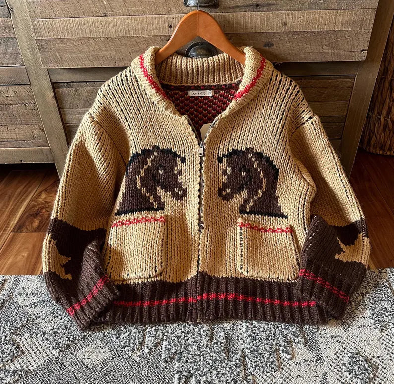Knitted sweater with horse designs on a wooden hanger against a wooden wall.