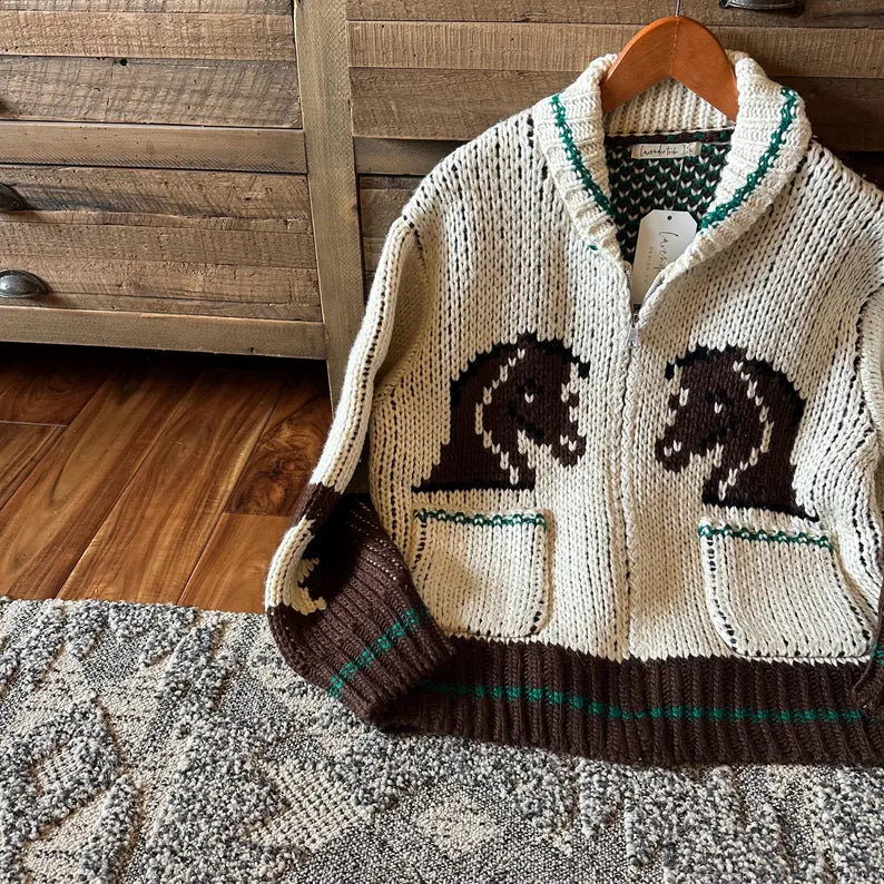 Knitted cardigan with horse designs on a wooden hanger against a wooden background