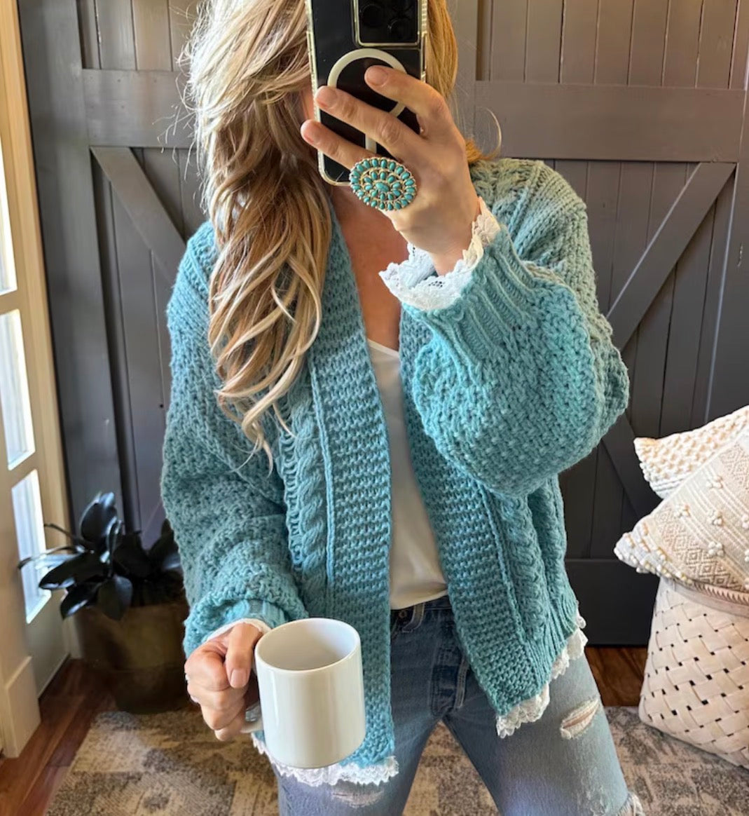 Woman wearing a light blue knitted cardigan holding a white mug indoors.
