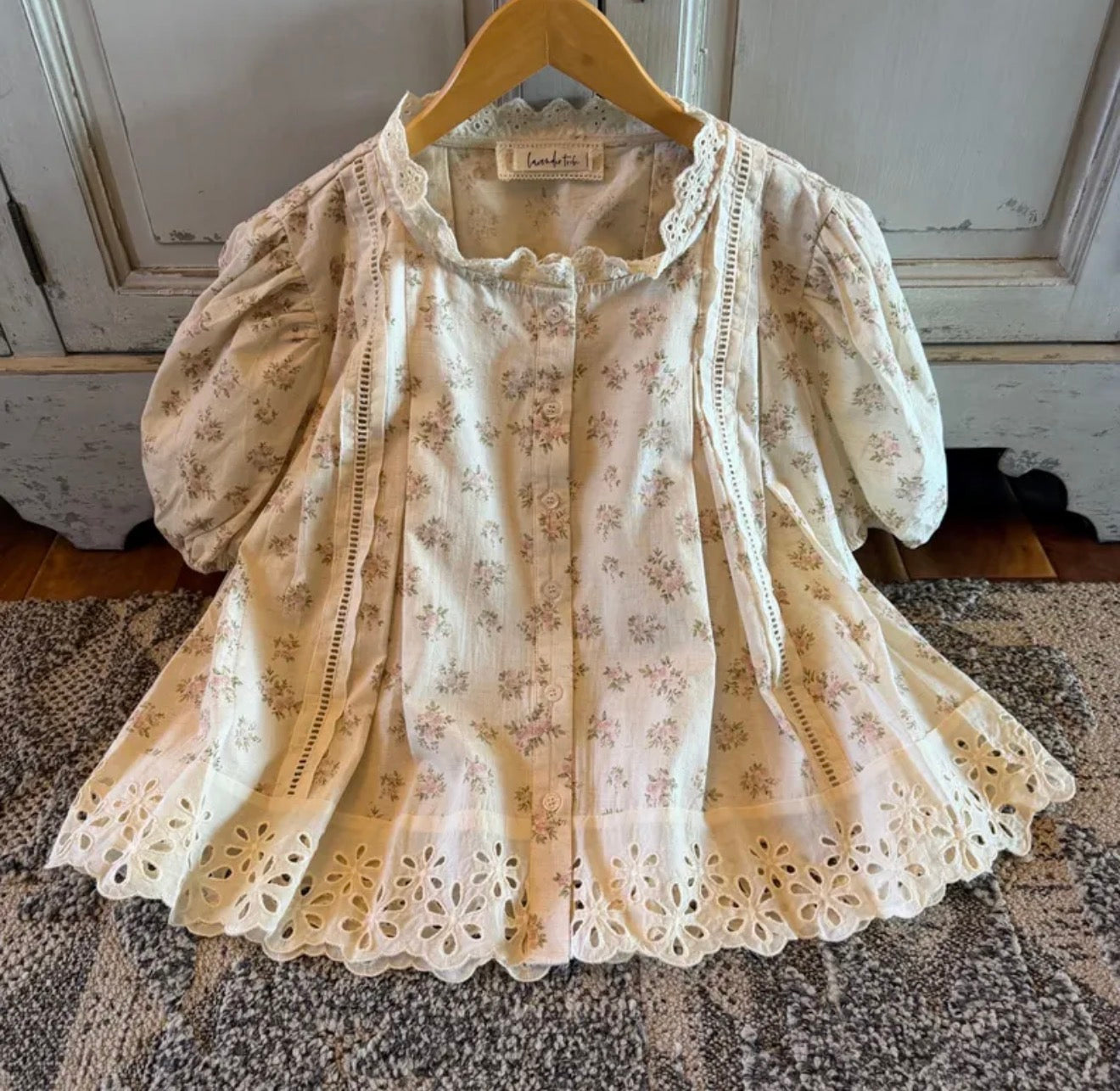 Floral lace blouse on a hanger against a wooden panel background