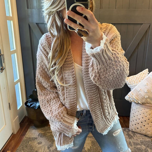 Person wearing a chunky knit beige cardigan in a home setting.
