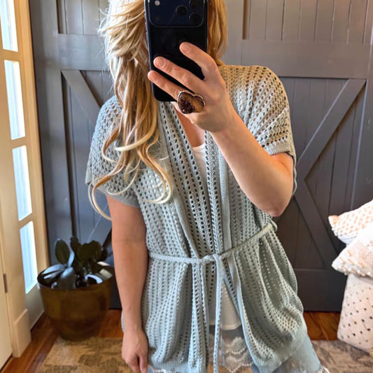 Person wearing a light gray crochet dress taking a mirror selfie.