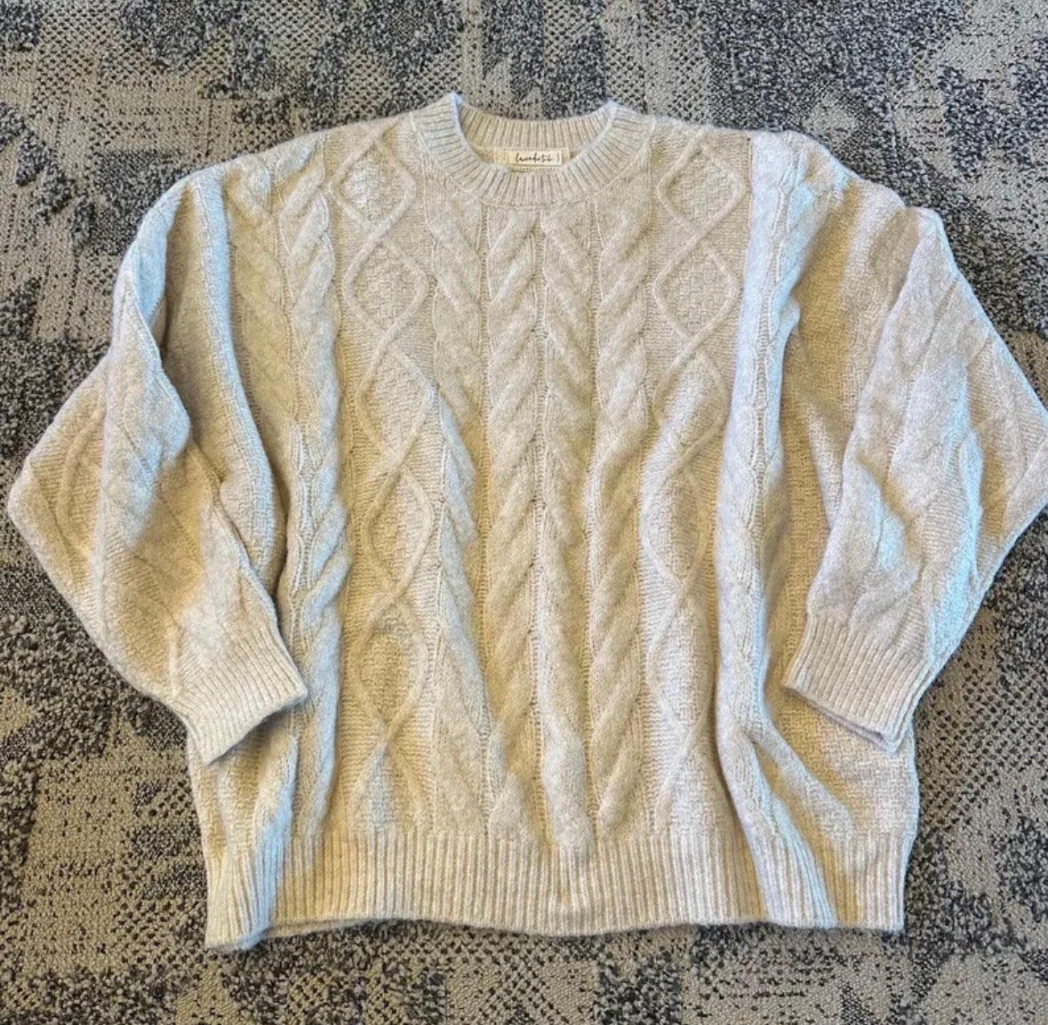 Beige cable knit sweater on a textured surface