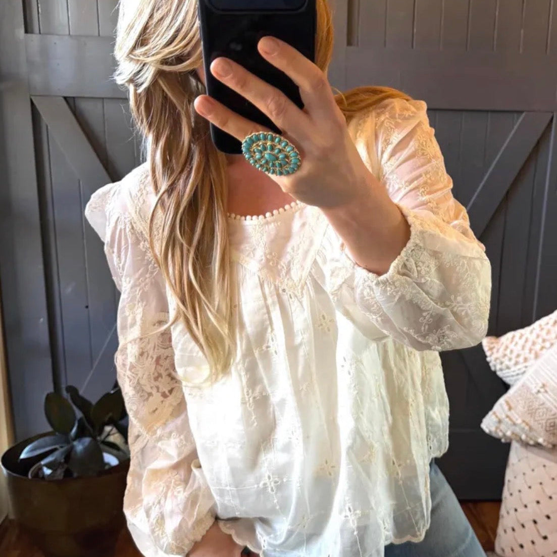 Person wearing a white lace top and blue jeans, taking a mirror selfie.