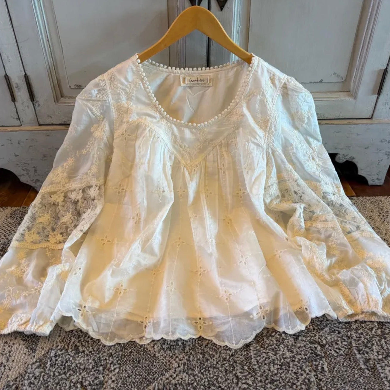 White lace blouse on a hanger against a neutral background