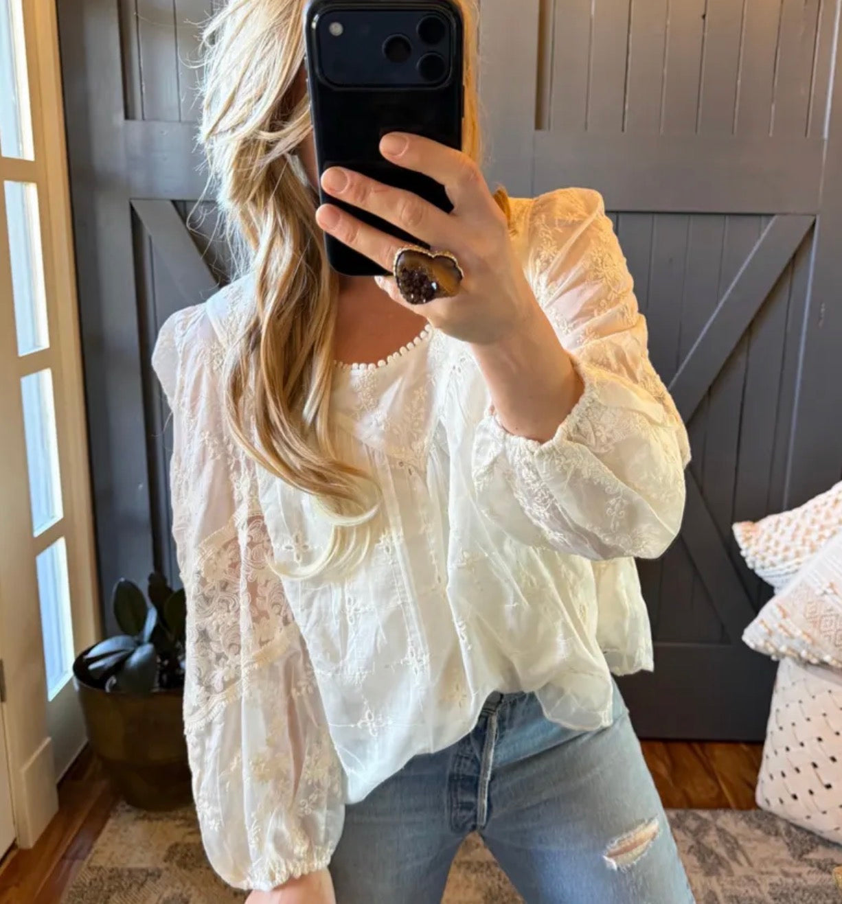 Person wearing a white blouse and blue jeans taking a mirror selfie.