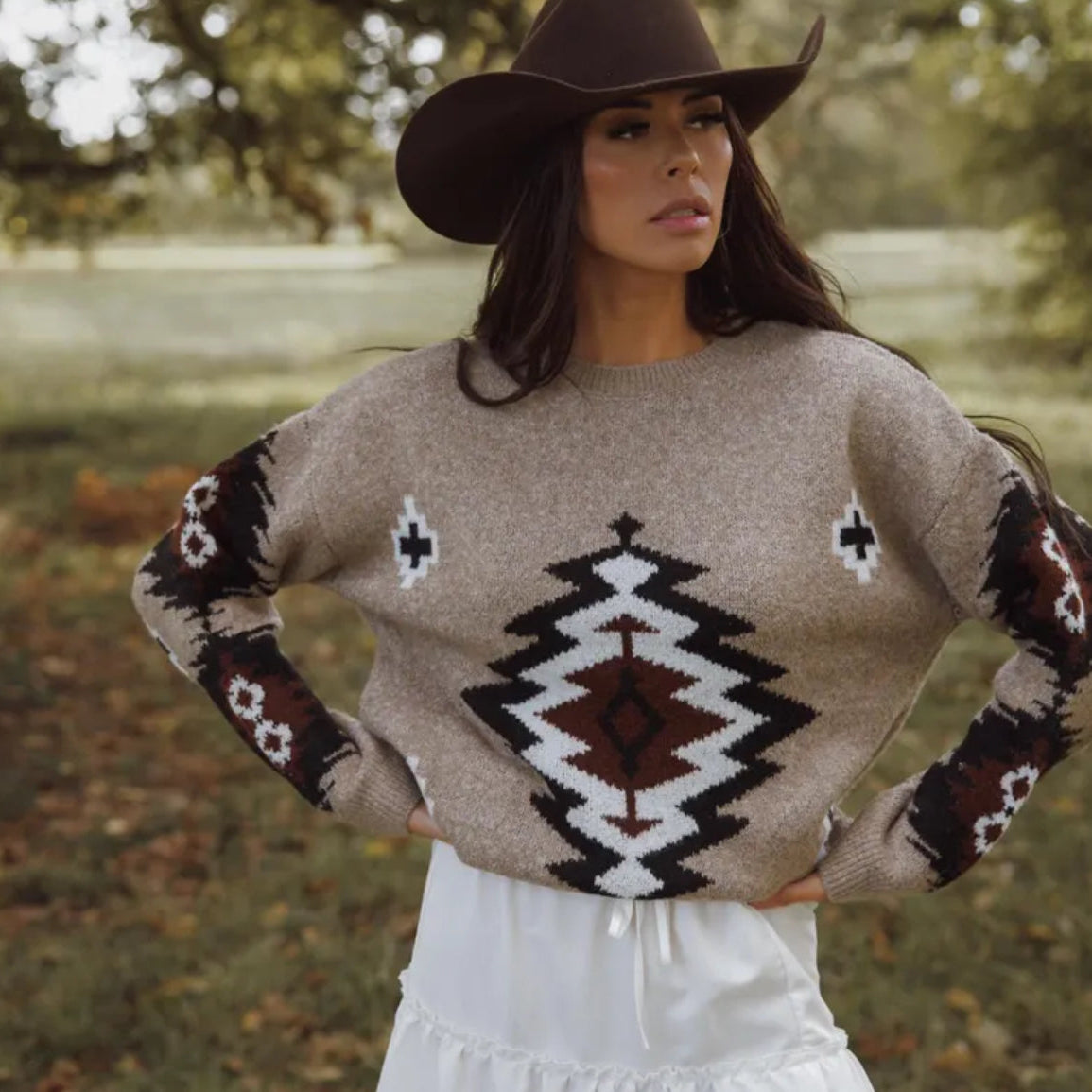 Woman wearing a patterned sweater and cowboy hat in an outdoor setting