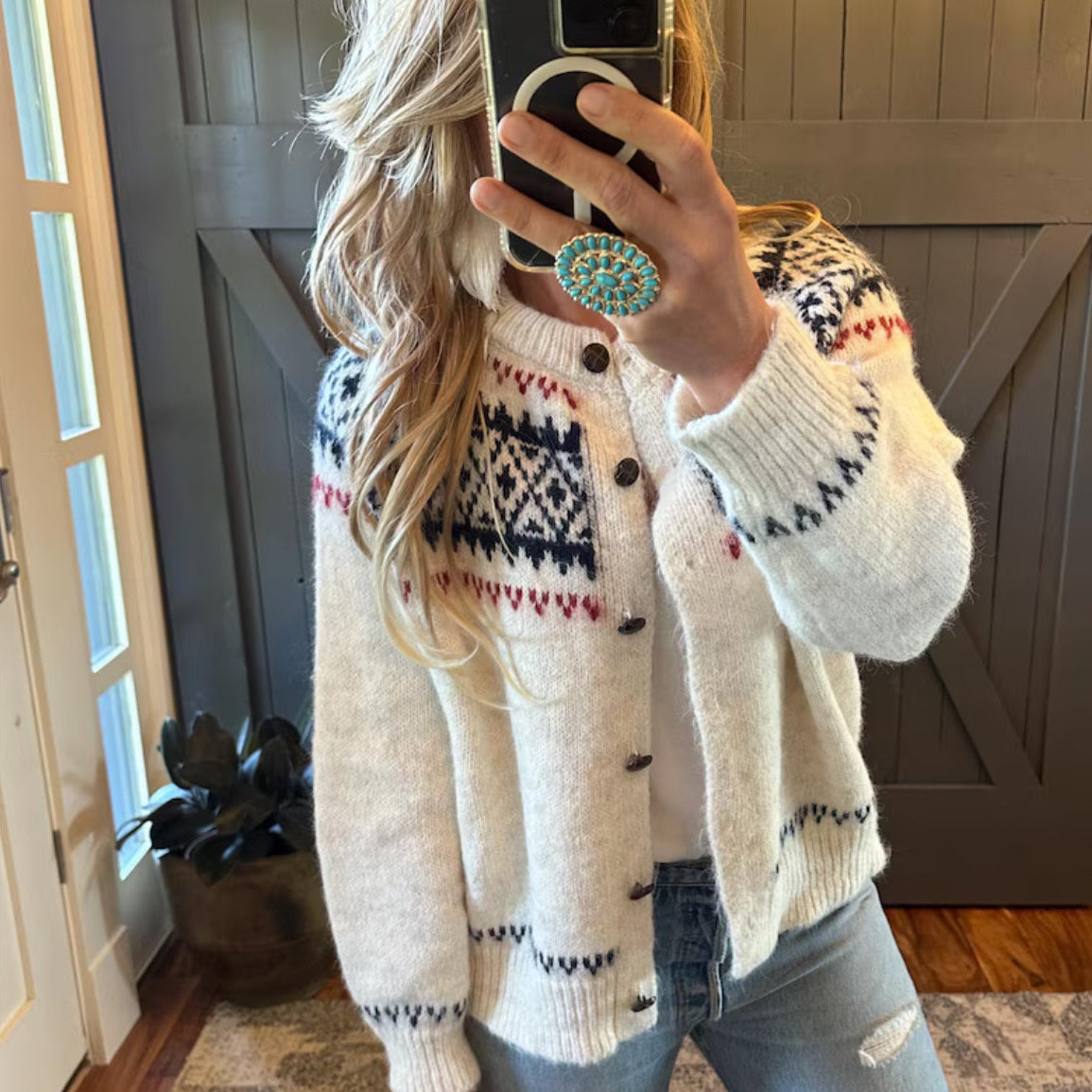 Person wearing a patterned cardigan taking a mirror selfie indoors.