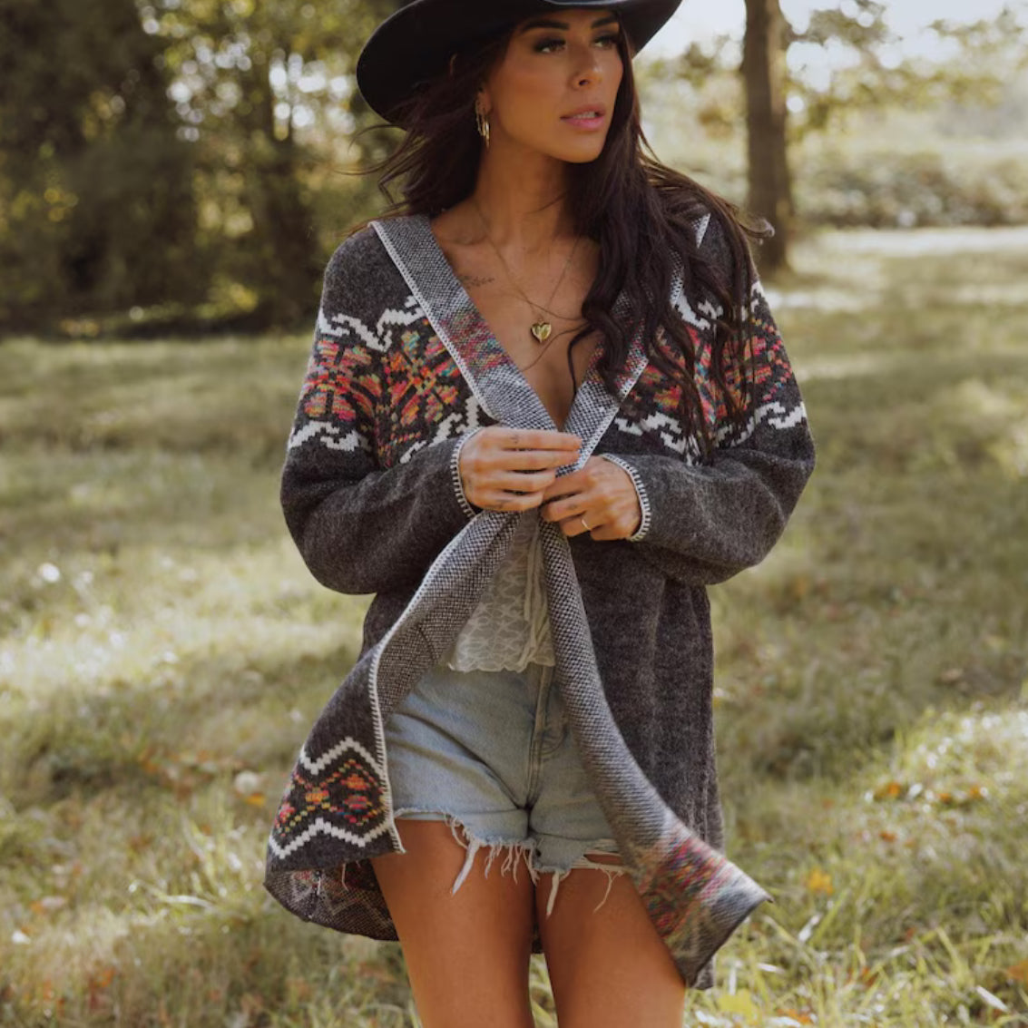 Woman wearing a patterned cardigan and denim shorts in a grassy field