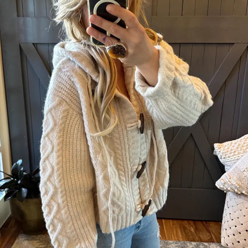 Person wearing a beige knitted cardigan taking a mirror selfie in a home setting.