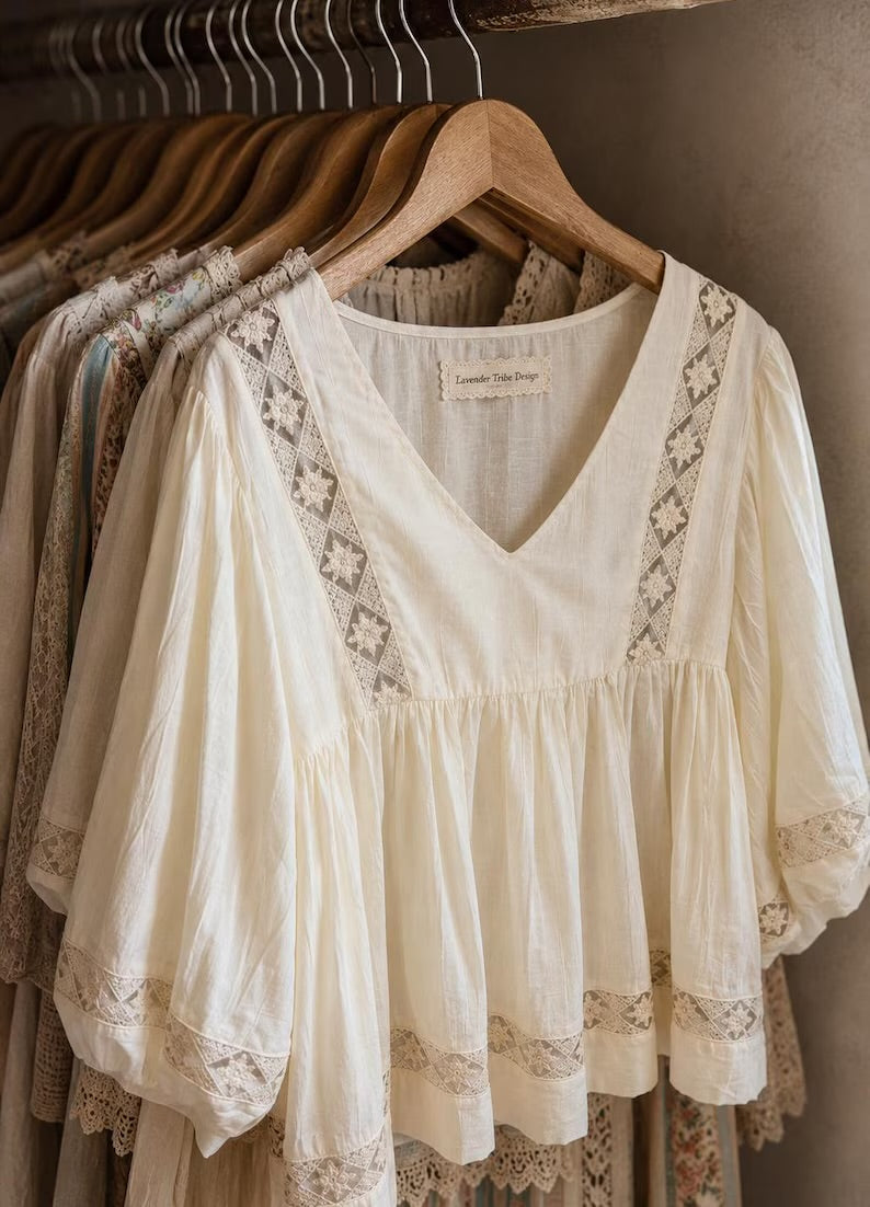 An off-white cotton blouse with lace trim and a V-neckline hanging on a wooden hanger in a closet setting.