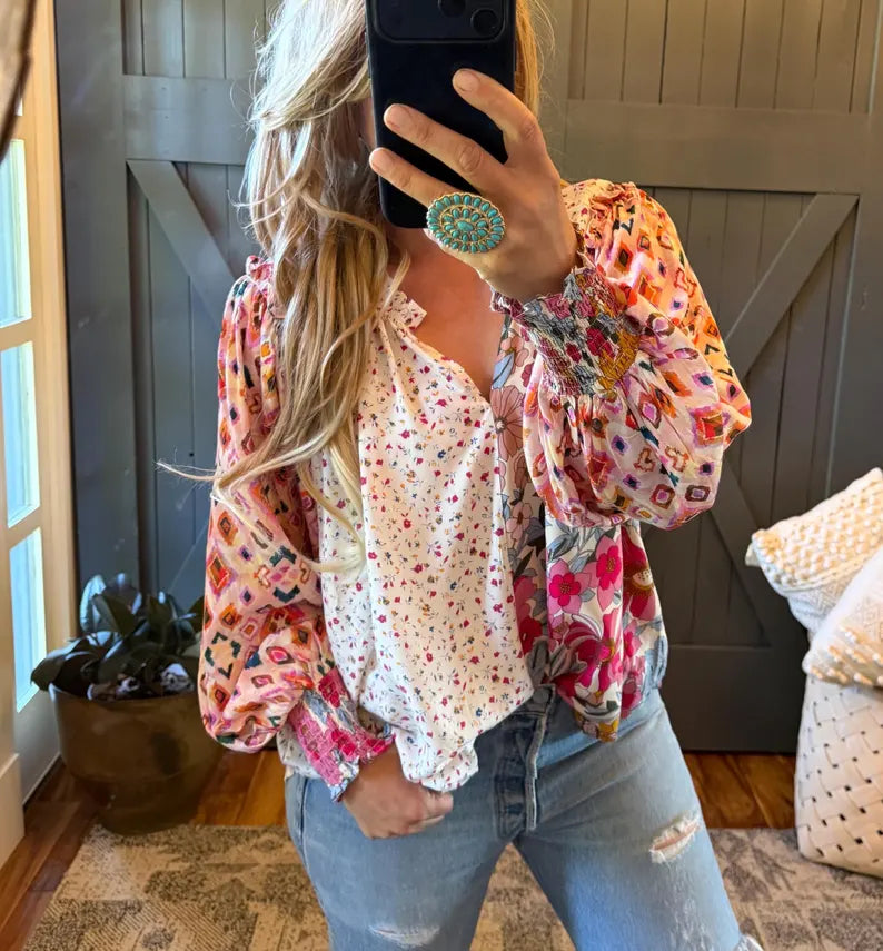 A woman takes a mirror selfie wearing a bohemian-style two-tone blouse with a white floral center and multicolor patterned sleeves, paired with light-wash distressed jeans.