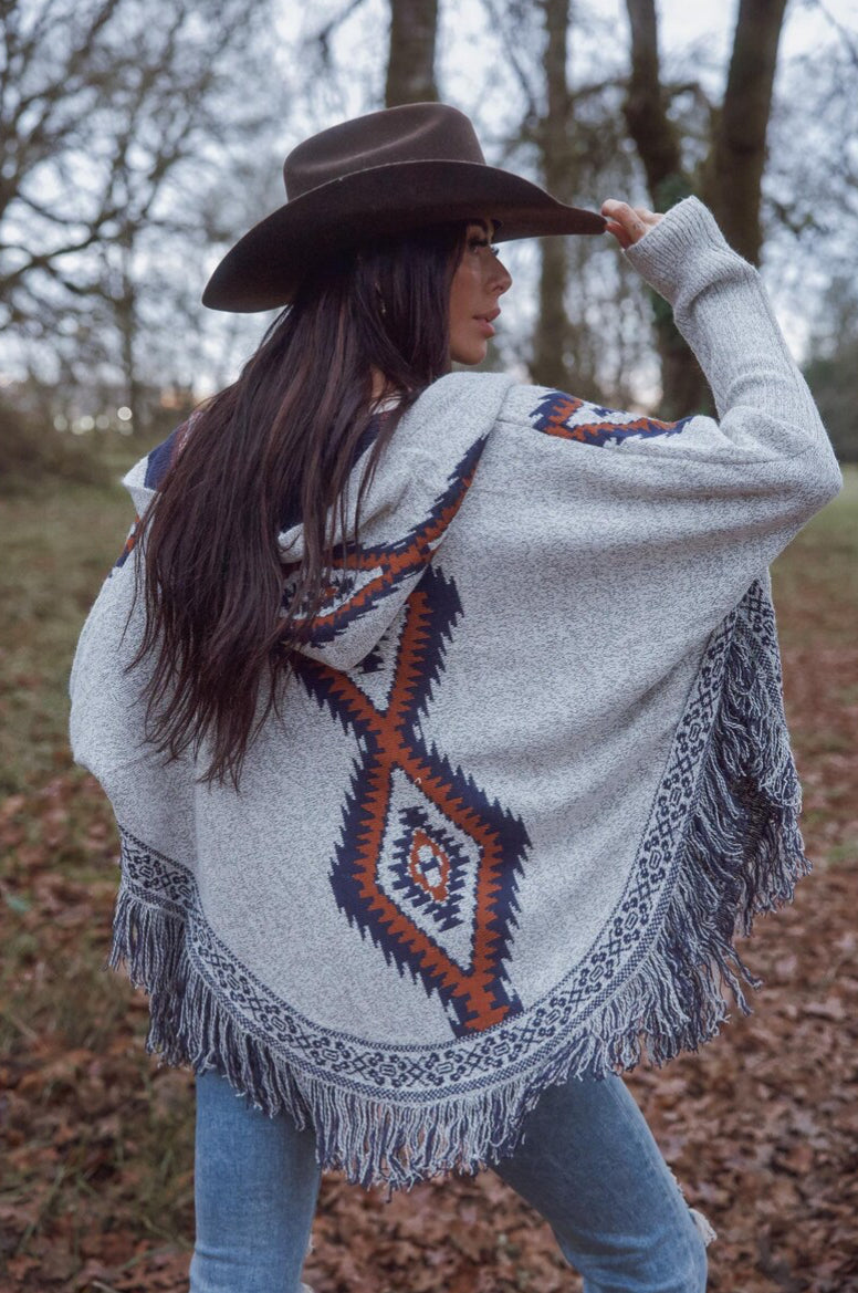 Woman wearing a patterned poncho and cowboy hat in an outdoor setting