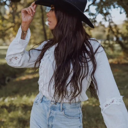 Woman wearing a white blouse with lace details and a black hat outdoors.