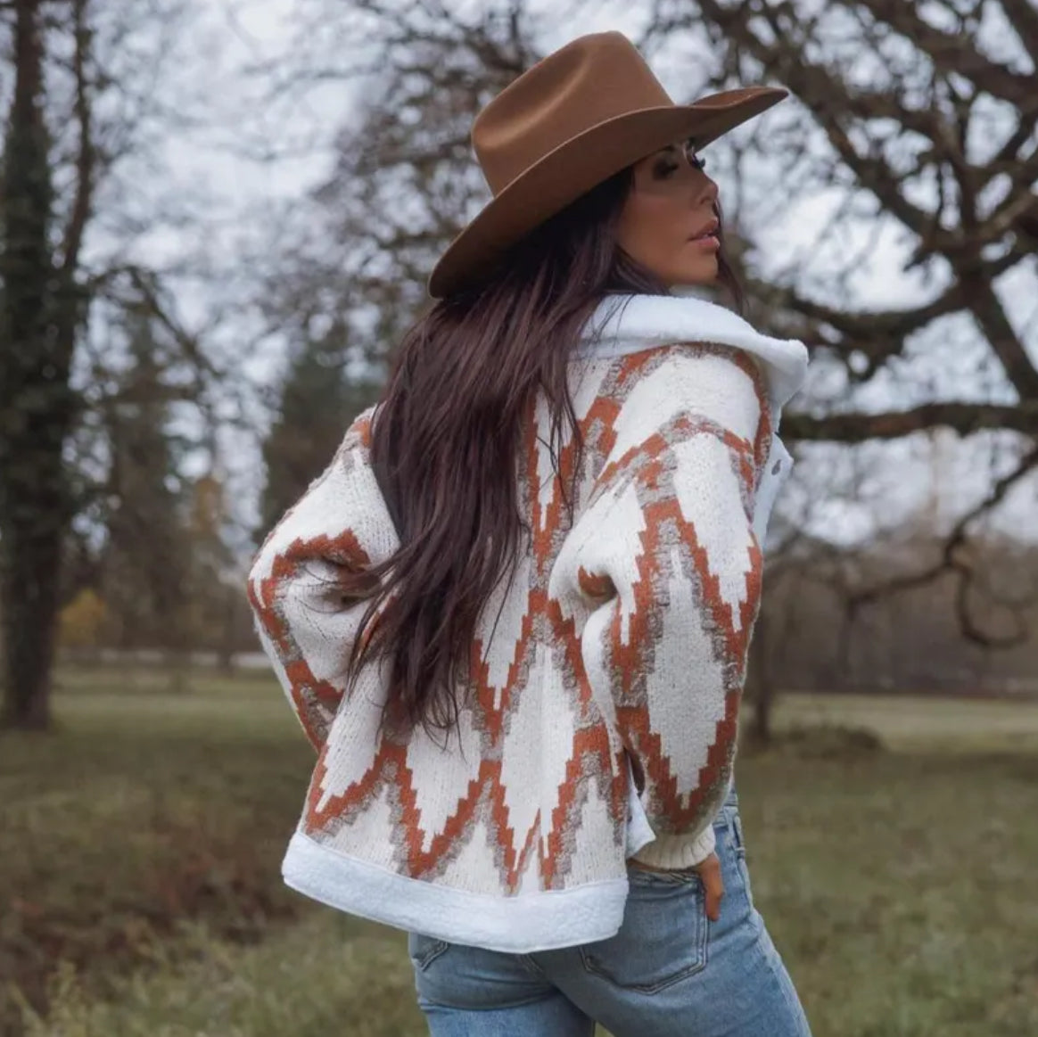 Woman wearing a patterned cardigan and brown hat in a natural setting