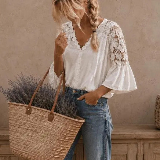 A woman stands barefoot in a rustic room, wearing a white lace-sleeve blouse and blue jeans, while carrying a large woven straw tote basket filled with lavender.