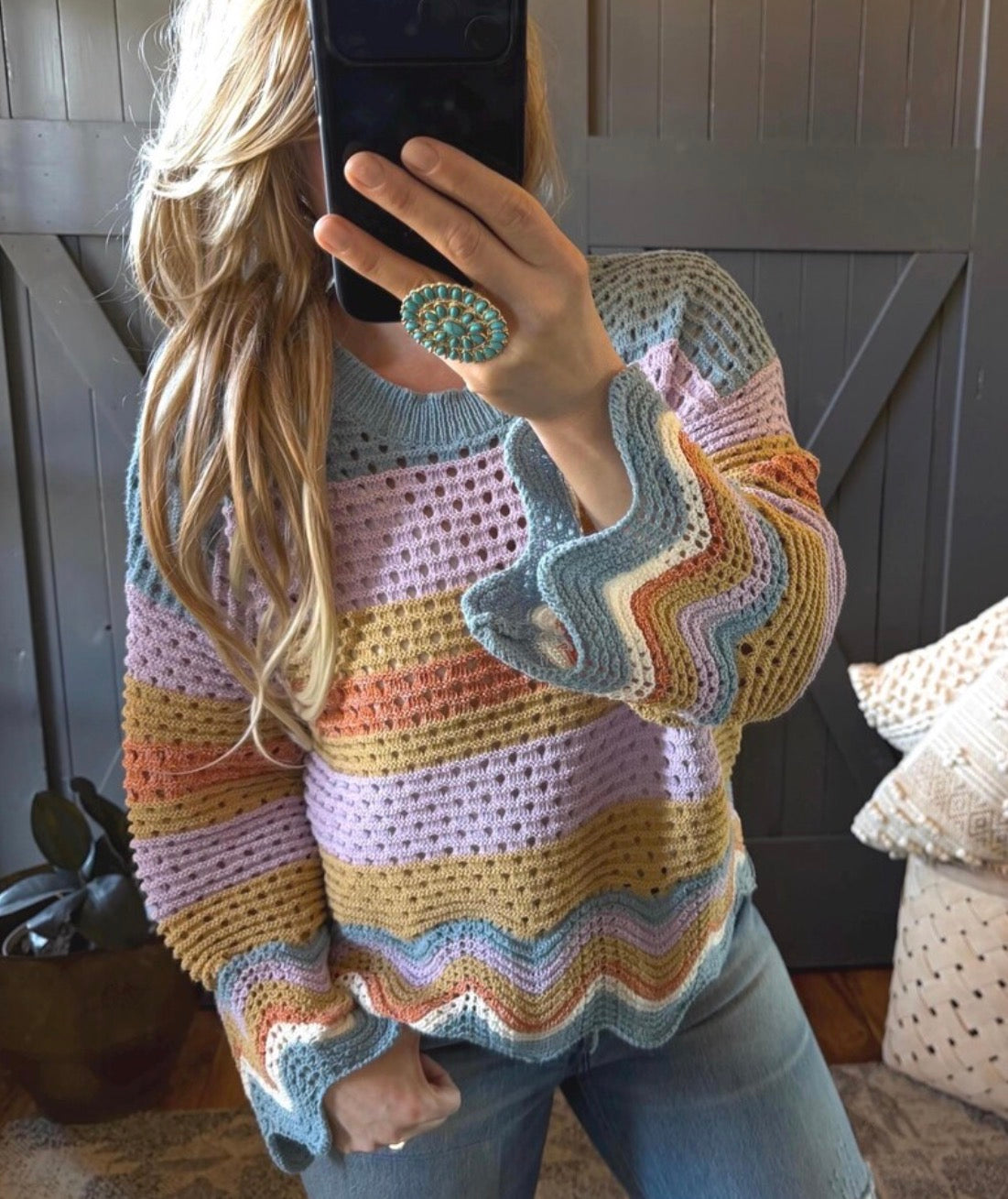 Person wearing a colorful striped sweater taking a mirror selfie.