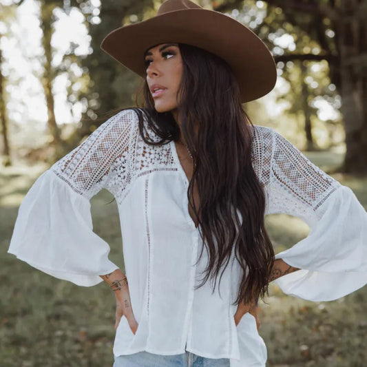 Woman wearing a white lace blouse and brown hat in a forest setting