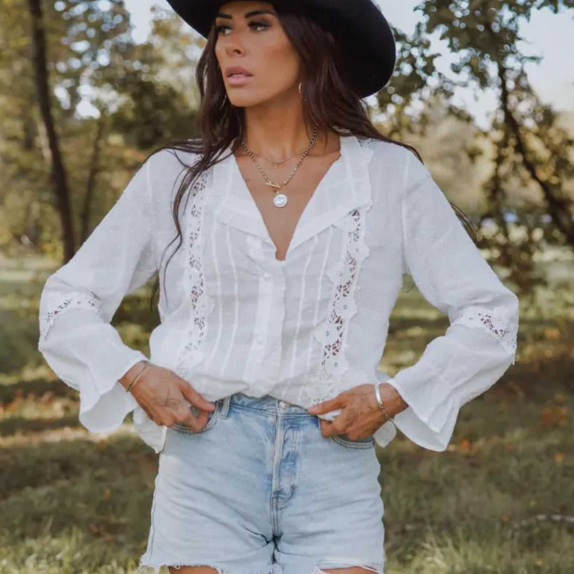 Woman wearing a white blouse with lace details and denim shorts in a natural setting.