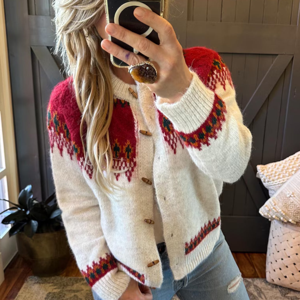 Person wearing a patterned cardigan taking a mirror selfie in a home setting.