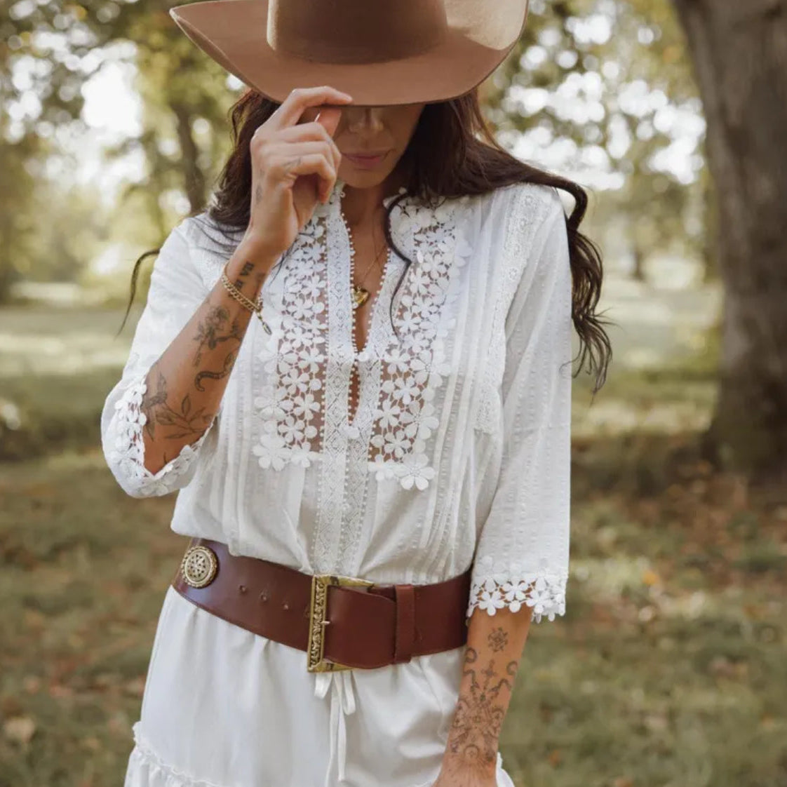 Woman wearing a white lace dress with a brown belt and hat in a park setting