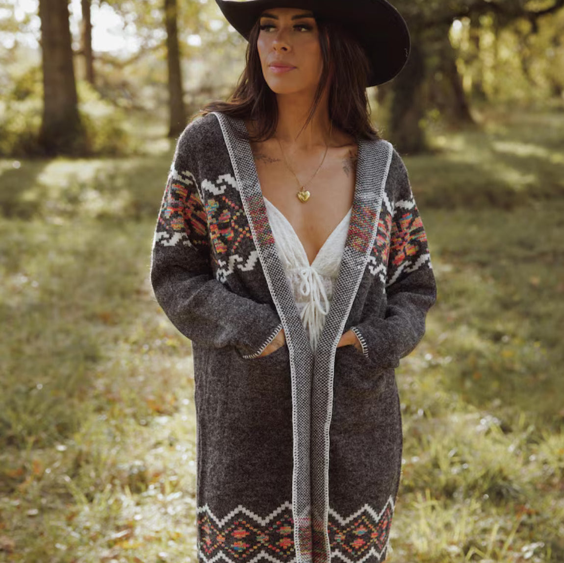 Woman wearing a patterned cardigan and hat in a forest setting