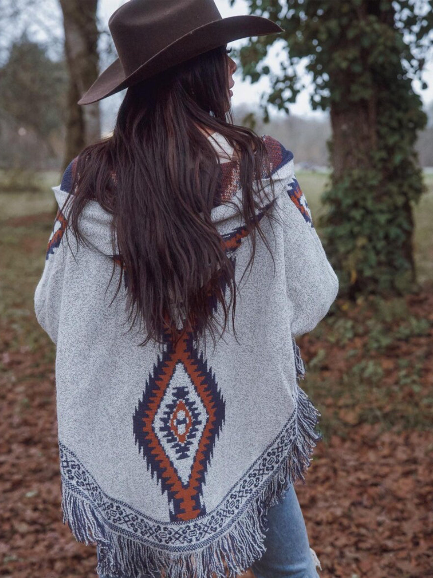 Person wearing a patterned poncho and brown hat in a natural setting