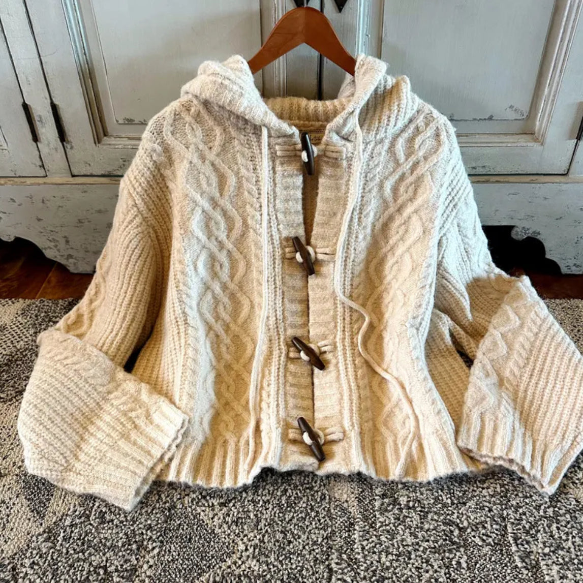 Beige knitted cardigan with button details on a wooden hanger against a neutral background