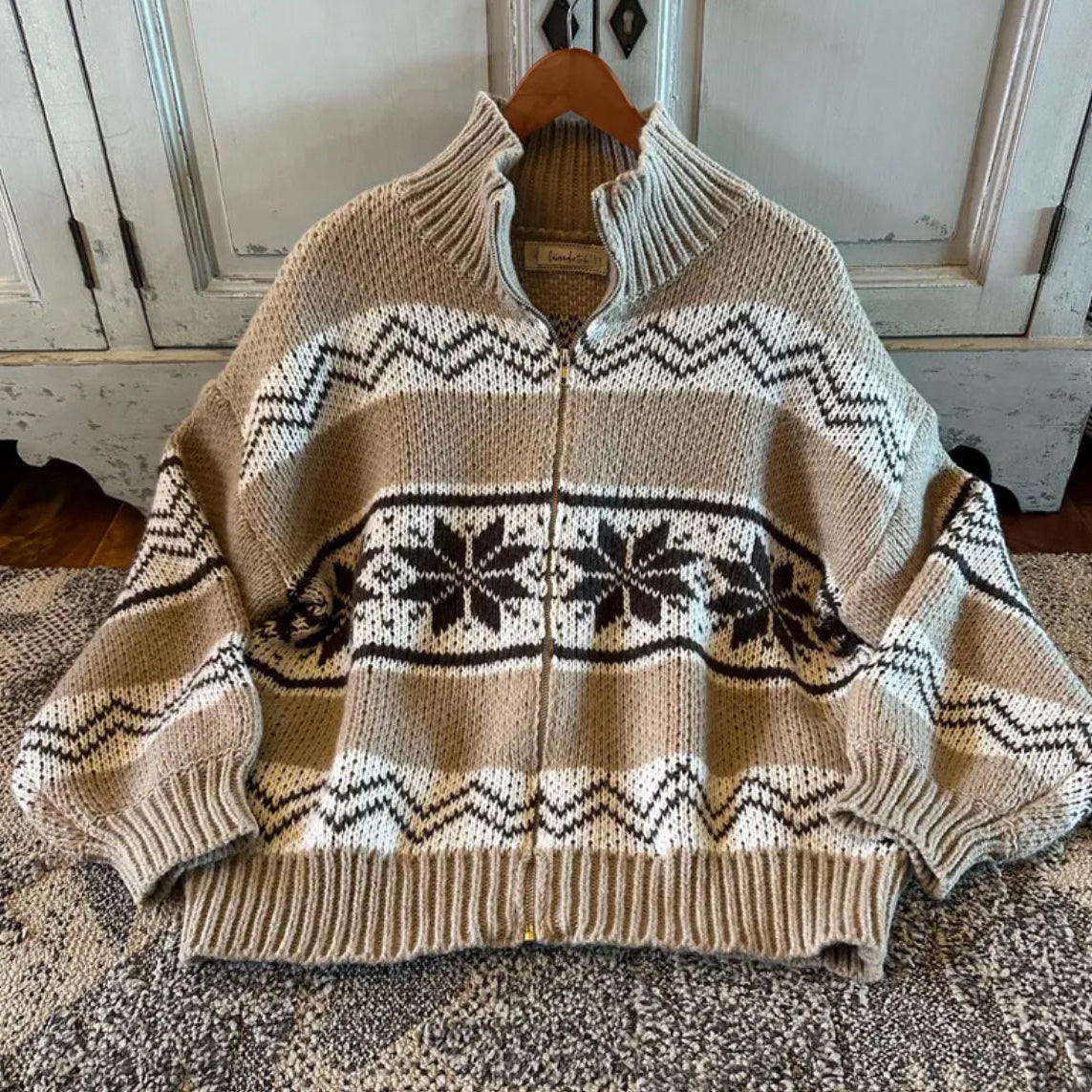 Beige sweater with a pattern on a hanger against a neutral background