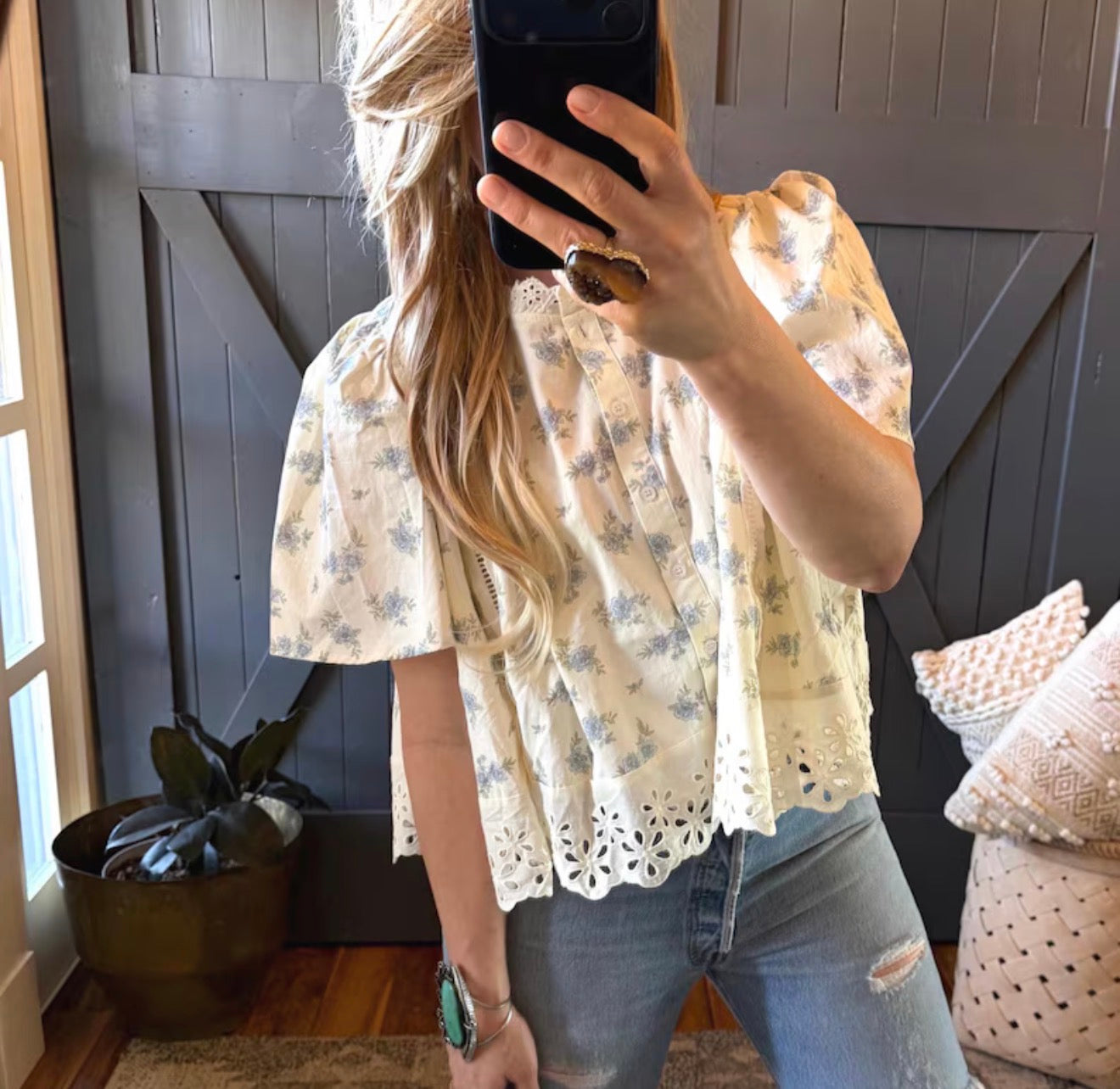 Person wearing a floral blouse and jeans taking a mirror selfie.