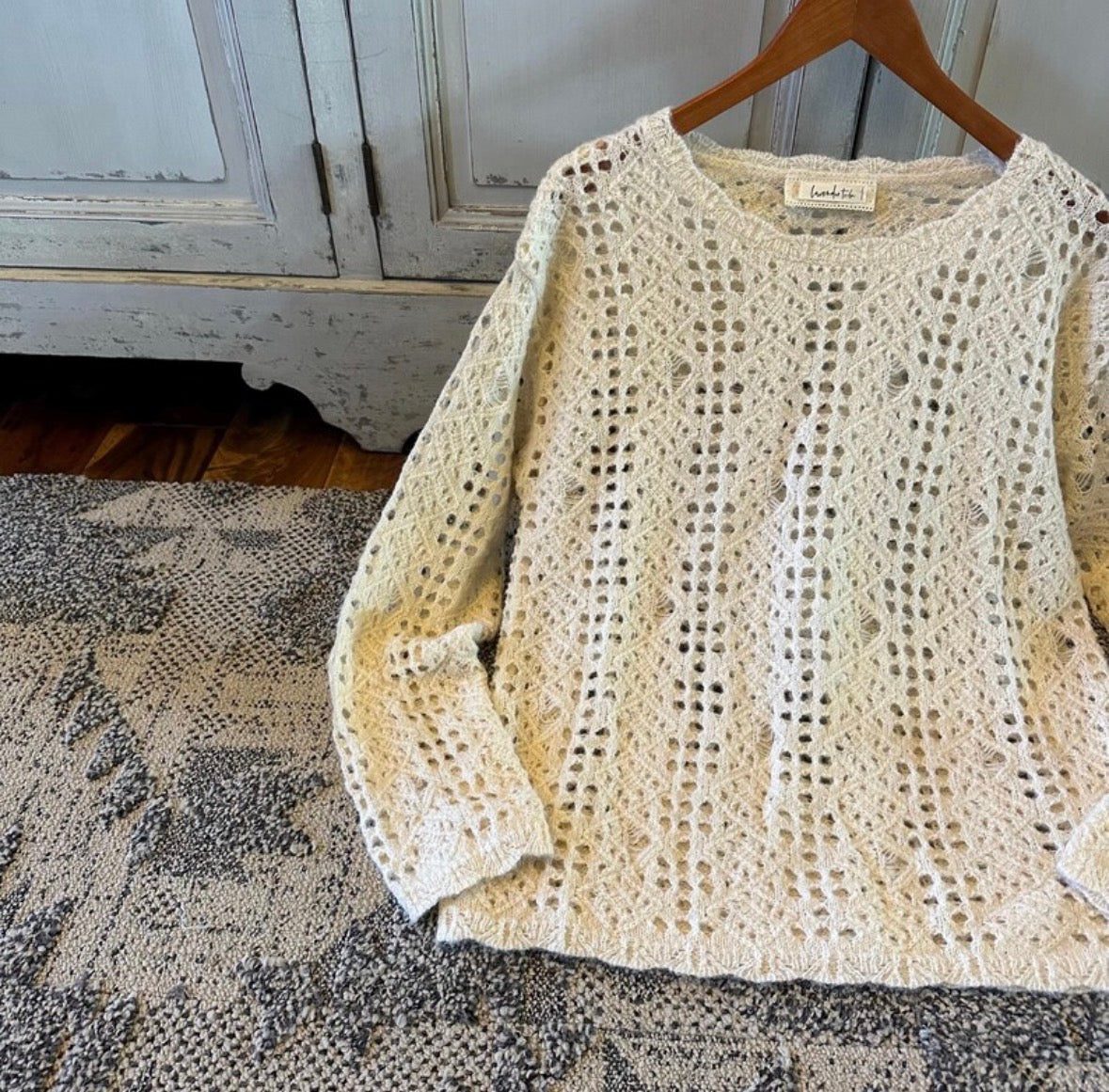 Beige crochet sweater on a wooden hanger against a rustic background