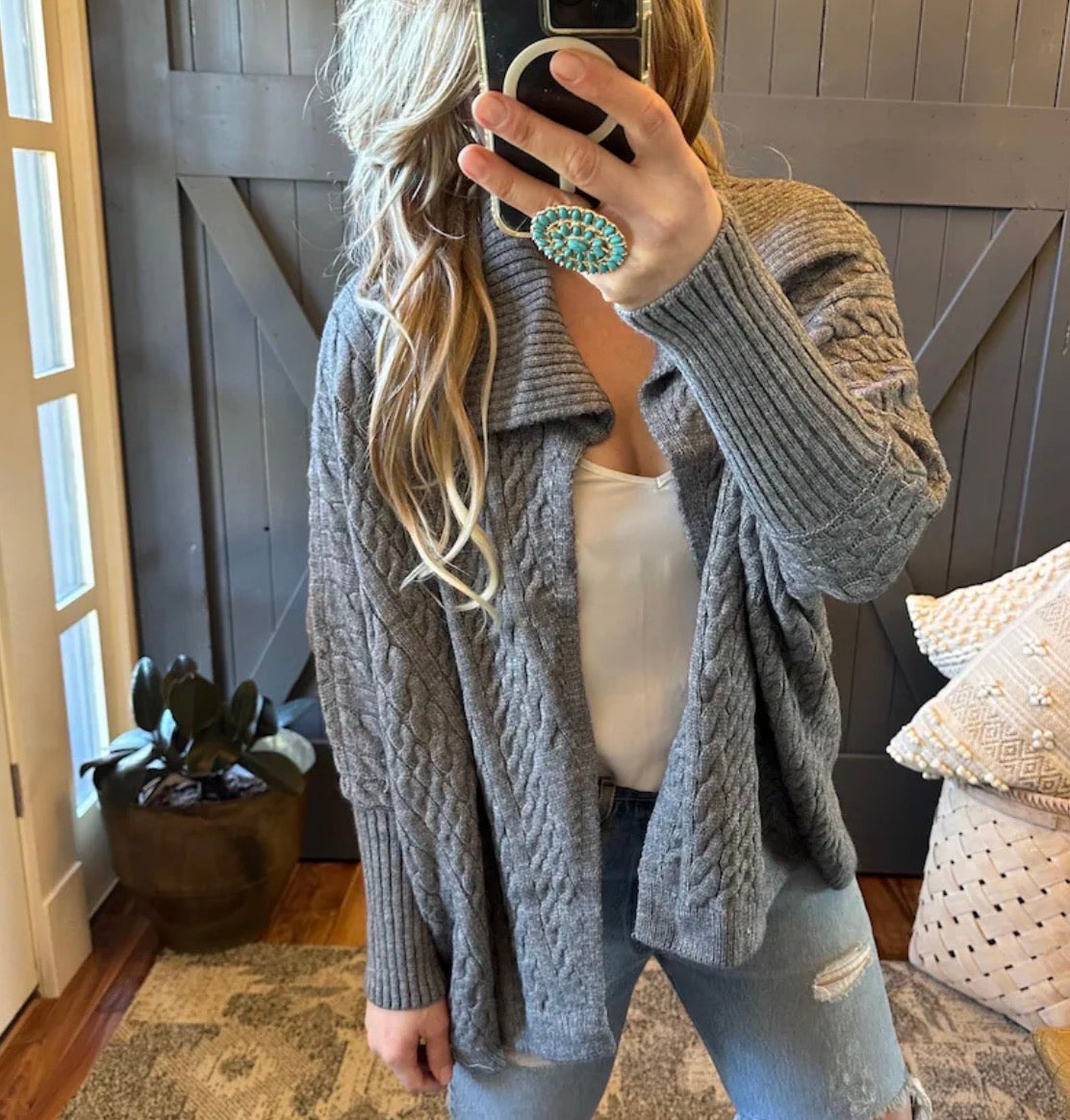 Person wearing a gray cable knit cardigan in a home setting