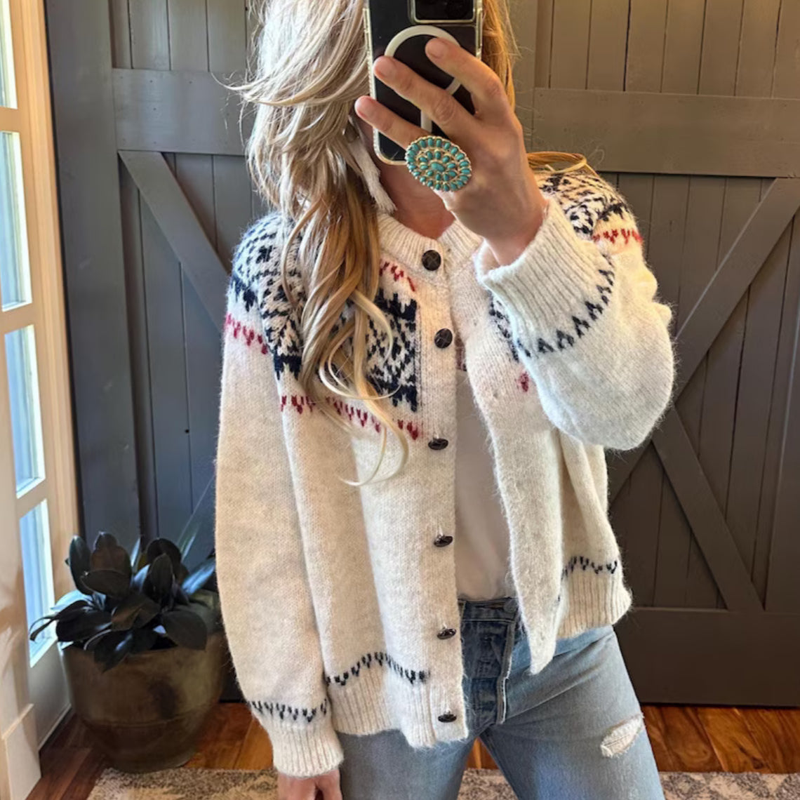 Person wearing a patterned cardigan taking a mirror selfie indoors.