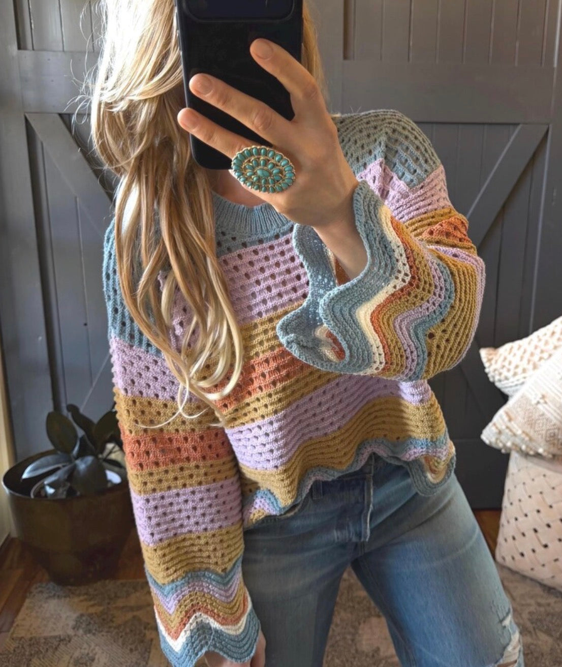 Person wearing a colorful crochet sweater taking a mirror selfie.